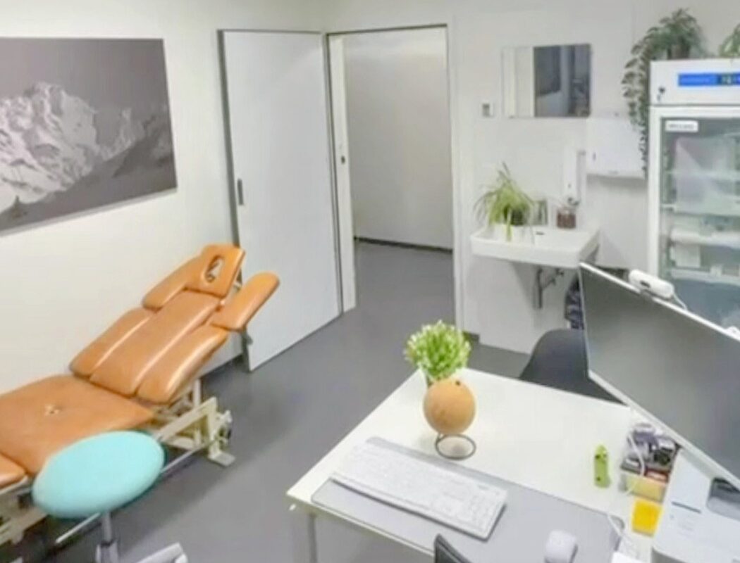 Cabinet médical moderne et lumineux avec table d’examen, bureau de consultation, plantes décoratives et réfrigérateur médical, dans un environnement calme et soigné.